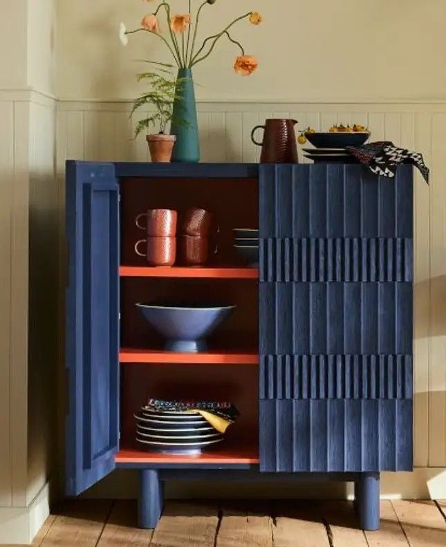 Navy blue cabinet with open doors displaying various ceramic items in a room.