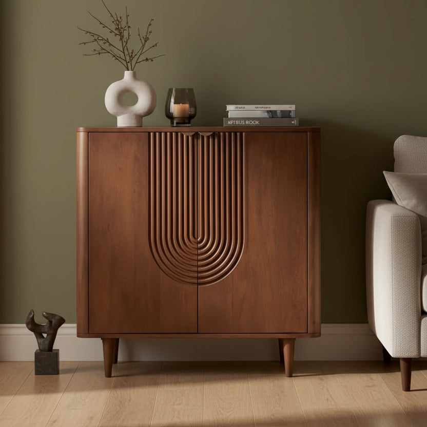 A mid-century modern wooden credenza or shoe cabinet with a carved arched detail on the front, styled in a warm room setting with a round mirror, vase, candle, and books on top by HOMELO