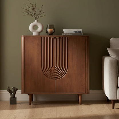 A mid-century modern wooden credenza or shoe cabinet with a carved arched detail on the front, styled in a warm room setting with a round mirror, vase, candle, and books on top by HOMELO