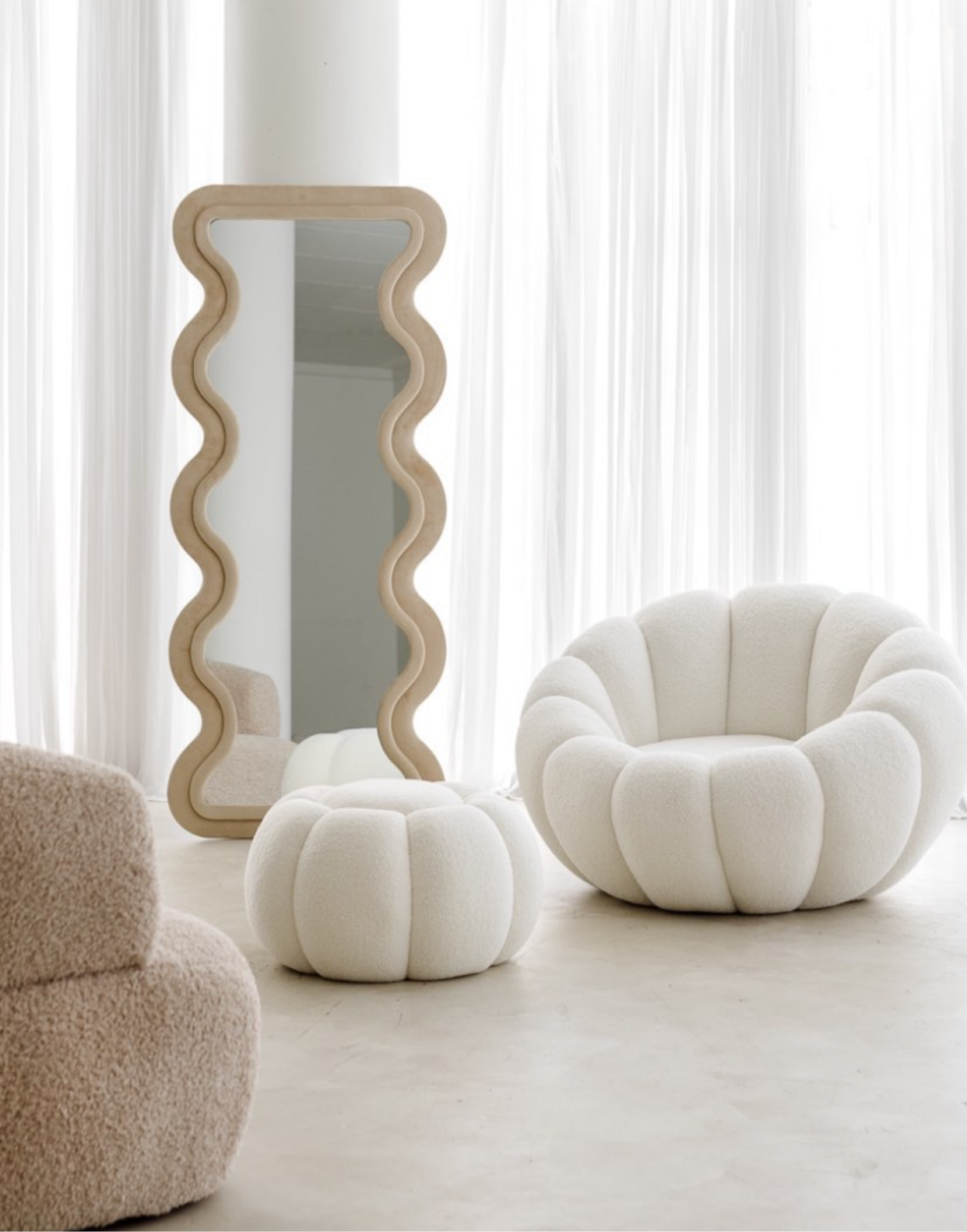 Pumpkin-shaped boucle chair with matching ottoman in soft white fabric, placed beside a wavy full-length mirror